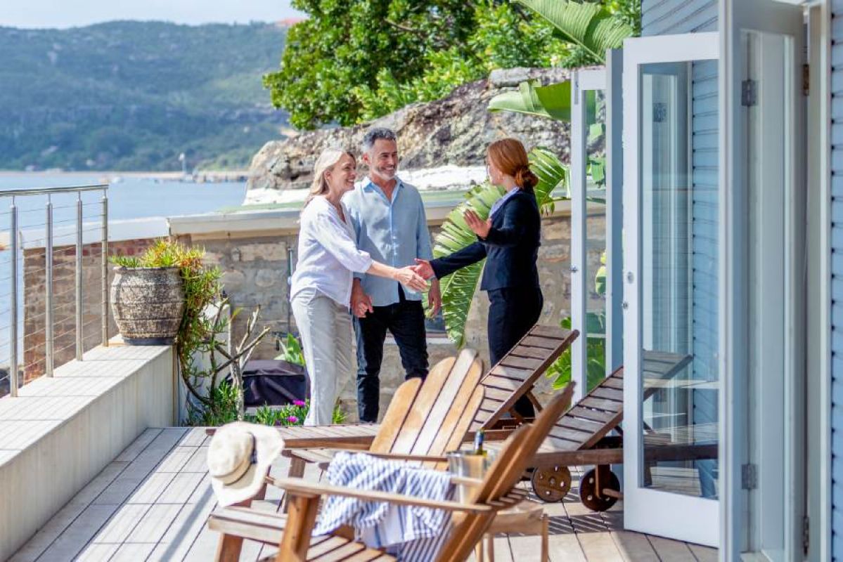 real estate agent shaking hands with older couple in porch of home fronting water