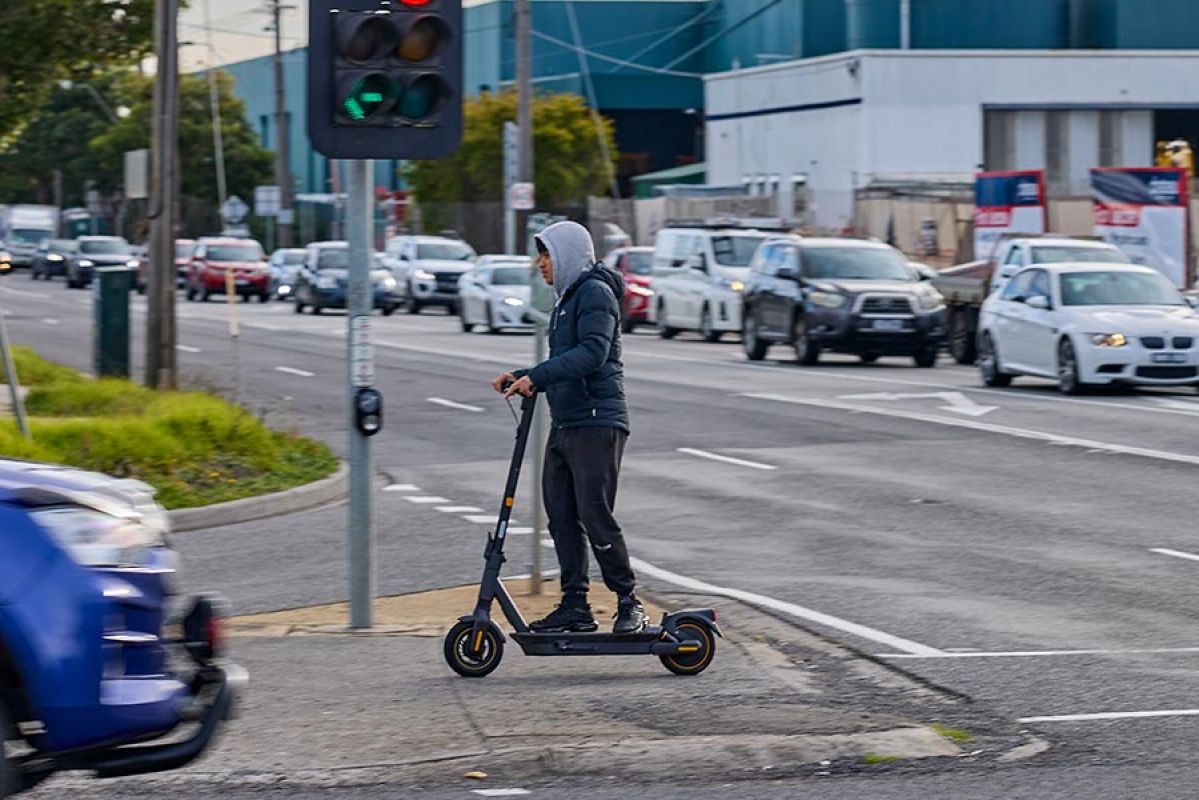 A young person riding an escooter across the intersection of Springvale Rd and Princes Highway in Mulgrave