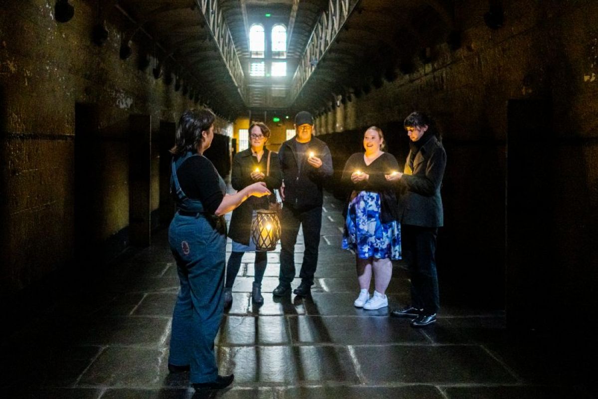 tour guide leading candlelit ghost tour in an old gaol with four guests